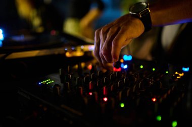 Bir gece kulübünde DJ 'lerin ellerinin mikser konsoluna yakın çekim, müzik ve dans atmosferi yaratıyorlar..
