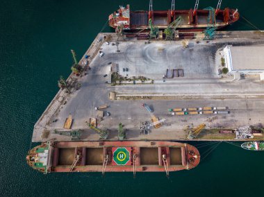 Büyük bir kargo gemisinin, bir hangar gemisinin buğday taneleriyle dolu olduğu hareketli bir limanın havadan üst görüntüsü.