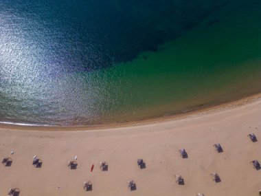 Saman şemsiyeleri, kızıl deniz kanosu ve sakin bir turkuaz deniz manzarası olan kumlu kumlu bir sahil manzarası.