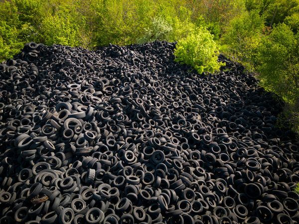 Вид сверху с воздуха резко контрастирует между массивной свалкой подержанных автомобильных шин и окружающими зелеными деревьями. Масштабы свалки шин поражают, подчеркивая негативное влияние отходов человека на окружающую среду.