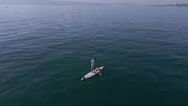 静かな海でスタンドアップパドルボードやSupボードをパドリングする男性の空中ビュー — ストック動画