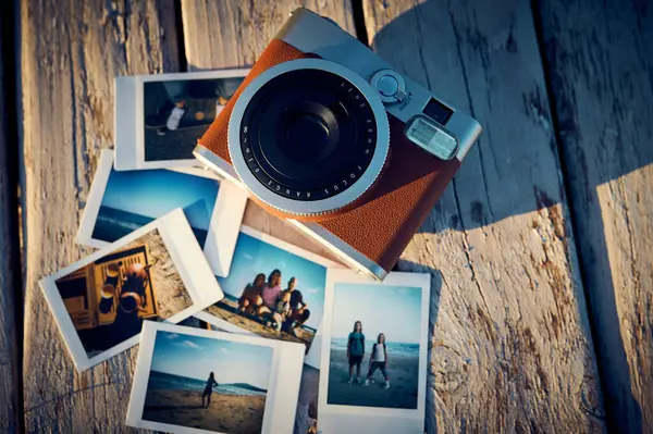 A vintage instant camera and several photographs lie on a old wooden table.