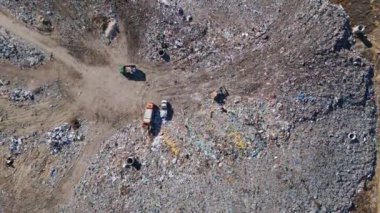 Buldozerlerin çalıştığı ve kamyonların yeni atıklar getirdiği uçsuz bucaksız bir arazi manzarası. Büyük kuş sürüleri olay yerinin üzerinde uçuyor..