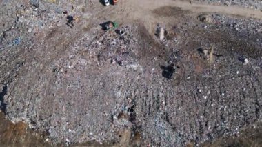 Buldozerlerin çalıştığı ve kamyonların yeni atıklar getirdiği uçsuz bucaksız bir arazi manzarası. Büyük kuş sürüleri olay yerinin üzerinde uçuyor..