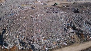 Buldozerlerin çalıştığı ve kamyonların yeni atıklar getirdiği uçsuz bucaksız bir arazi manzarası. Büyük kuş sürüleri olay yerinin üzerinde uçuyor..