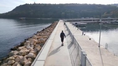 Bir adam deniz kenarındaki bir güvertede uzun bir sörf tahtasına biniyor, İHA 'dan görülüyor..