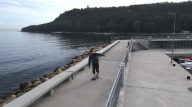 Bir adam deniz kenarındaki bir güvertede uzun bir sörf tahtasına biniyor, İHA 'dan görülüyor..