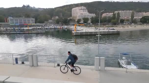一个背着背包的男人骑着自行车沿着海滨长廊 从一架无人驾驶飞机上看到了他 — 图库视频影像
