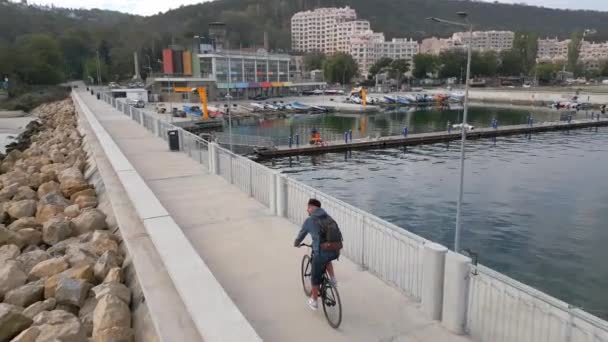 Seorang Pria Dengan Ransel Mengendarai Sepeda Sepanjang Jalan Tepi Laut — Stok Video