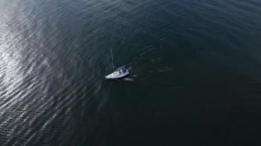 Motoru çalışır vaziyette denizde yelken açan bir yat rüzgarsız havada, hava manzaralı bir yerde denize açılır.