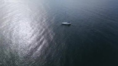 Motoru çalışır vaziyette denizde yelken açan bir yat rüzgarsız havada, hava manzaralı bir yerde denize açılır.