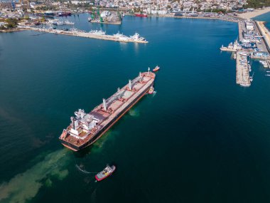 Büyük bir kargo gemisi, römorkör ve hava manzarasıyla birlikte limandan ayrılıyor..