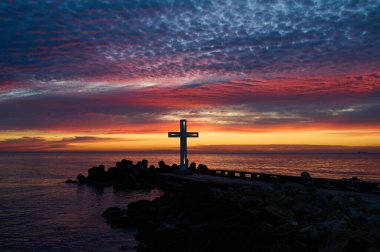 Hıristiyan haçı sabahın erken saatlerinde gün doğumunda. Büyük haç, deniz kıyısındaki dalgakıranın kenarında duruyor..