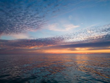 Sabahın erken saatlerinde, yükselen güneş ve renkli gökyüzü ile denizin üzerinde uçan bir dronun görüntüsü..