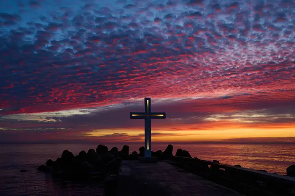 Christian cross early in the morning at sunrise. The large cross stands on the edge of a breakwater on the sea coast.