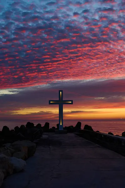 Christian cross early in the morning at sunrise. The large cross stands on the edge of a breakwater on the sea coast.