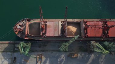 Aerial view of big cargo ship bulk carrier is loaded with grain of wheat in port at sunset.