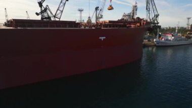 Aerial view of big cargo ship bulk carrier is loaded with grain of wheat in port at sunset.