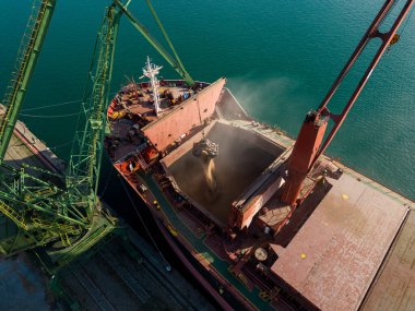 Aerial view of big cargo ship bulk carrier is loaded with grain of wheat in port at sunset.