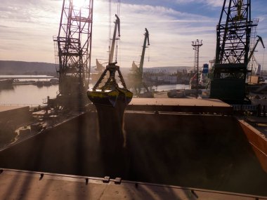 Aerial view of big cargo ship bulk carrier is loaded with grain of wheat in port at sunset.