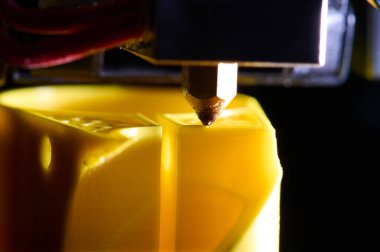 3D yazıcı, sarı plastikten yapılmış bir parça yazdırıyor, yakın plan görünüm.