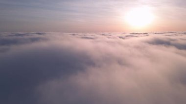 Uçsuz bucaksız kabarık bulutların üzerinde yükselen güneşin sakin bir drone görüntüsü..