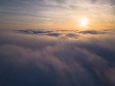 Uçsuz bucaksız kabarık bulutların üzerinde yükselen güneşin sakin bir drone görüntüsü..