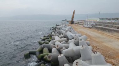 Kumlu sahil boyunca uzanan uzun beton bloklar kıyıda görünür bir sınır oluşturuyor..