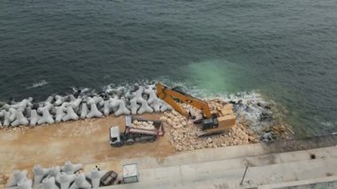 Kumlu sahil boyunca uzanan uzun beton bloklar kıyıda görünür bir sınır oluşturuyor..