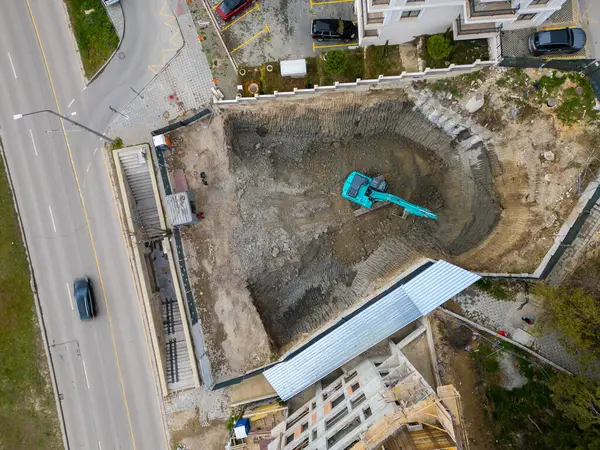 stock image A bulldozer is digging a pit for the construction of another building in the middle of the city, aerial view.