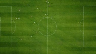 Futbol sahasının havadan görünüşü, oyuncular koşuyor, pas veriyor ve gol atıyor.