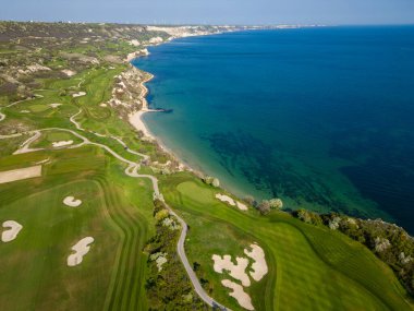 Okyanus yakınlarındaki yemyeşil golf sahasının kuş bakışı manzarası. Kum tuzakları ve su tehlikeleri görülebiliyor..