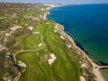 Okyanus yakınlarındaki bir golf sahasının hava perspektifinde yemyeşil otlaklar ve kum tuzakları sergileniyor..