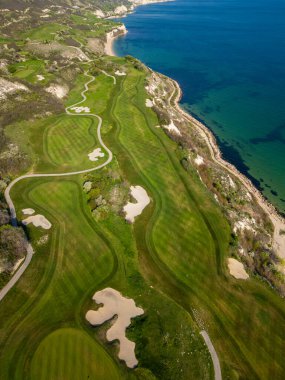 Okyanus yakınlarındaki bir golf sahasının hava perspektifinde yemyeşil otlaklar ve kum tuzakları sergileniyor..