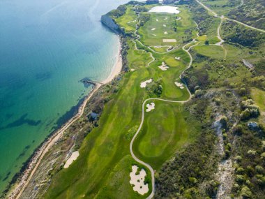 Okyanusun yanındaki bir golf sahasının kuş bakışı görüntüsü, yeşil çayırları ve deniz zeminindeki kum tuzaklarını gösteriyor..