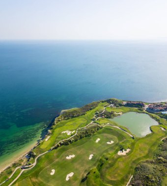 Okyanusun arka planına karşı kurulmuş yüksek açılı bir golf sahası, yemyeşil otlaklar ve kum tuzakları sergiliyor..