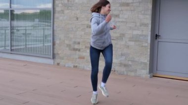 Günlük giysiler içinde, kot pantolon ve süveter giyen kaygısız genç bir kadın neşeyle sokakta zıplıyor..