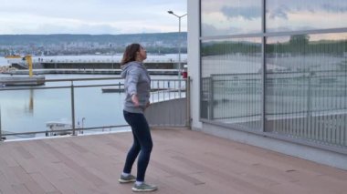 Günlük giysiler içinde, kot pantolon ve kazak giyen genç bir kadın, şehirde doğu sağlığı egzersizi qigong pratik yapıyor..