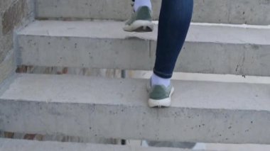 Kot pantolon ve spor ayakkabı giymiş bir kadının bacakları merdivenleri çıkarken, arkadan yakın plan..