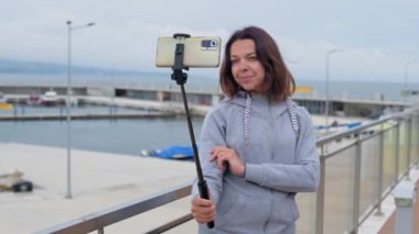 Genç bir kadın akıllı telefon ve selfie çubuğu kullanarak mutlu bir şekilde iletişim kuruyor..