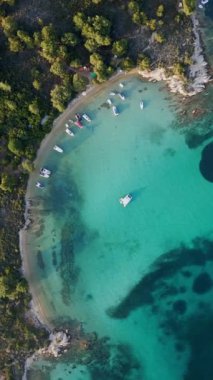 Yunanistan 'ın Sithonia Yarımadası' nda kristal berrak sularla çevrili plajları ve kayaları olan bir adanın havadan görünüşü. Yatlar ve tekneler turkuaz sularda demirliyor. Yakındaki adalar ve resifler görülebilir..