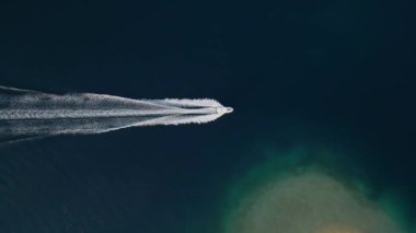 Sakin, koyu mavi okyanusta hızla ilerleyen bir teknenin havadan görünüşü ardında beyaz dalgalar bırakıyor. Uçsuz bucaksız denizin basitliği ve sükuneti teknelerin hareketleriyle tezat oluşturuyor..