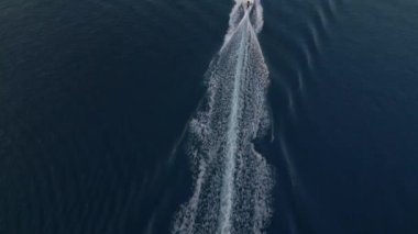 Sakin, koyu mavi okyanusta hızla ilerleyen bir teknenin havadan görünüşü ardında beyaz dalgalar bırakıyor. Uçsuz bucaksız denizin basitliği ve sükuneti teknelerin hareketleriyle tezat oluşturuyor..