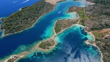 Yunanistan 'ın Sithonia Yarımadası' nda kristal berrak sularla çevrili plajları ve kayaları olan bir adanın havadan görünüşü. Yatlar ve tekneler turkuaz sularda demirliyor. Yakındaki adalar ve resifler görülebilir..