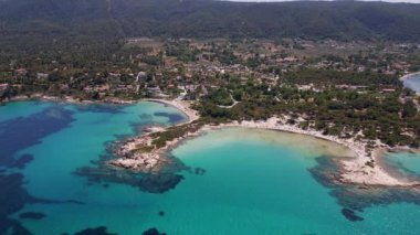 Yunanistan 'ın Sithonia Yarımadası' nda kristal berrak sularla çevrili plajları ve kayaları olan bir adanın havadan görünüşü. Yatlar ve tekneler turkuaz sularda demirliyor. Yakındaki adalar ve resifler görülebilir..