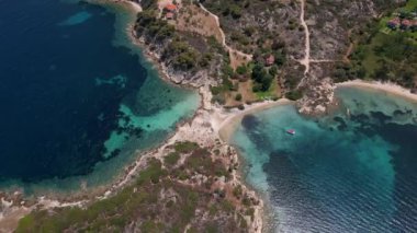 Yunanistan 'ın Sithonia Yarımadası' nda kristal berrak sularla çevrili plajları ve kayaları olan bir adanın havadan görünüşü. Yatlar ve tekneler turkuaz sularda demirliyor. Yakındaki adalar ve resifler görülebilir..