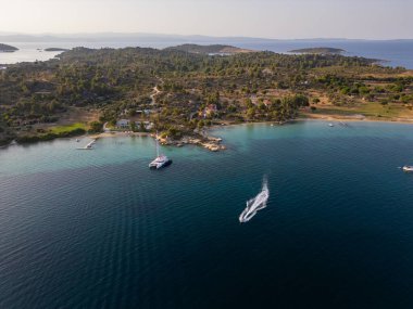 Yunanistan 'ın Sithonia Yarımadası' nda kristal berrak sularla çevrili plajları ve kayaları olan bir adanın havadan görünüşü. Yatlar ve tekneler turkuaz sularda demirliyor. Yakındaki adalar ve resifler görülebilir..