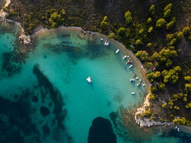 Yunanistan 'ın Sithonia Yarımadası' nda kristal berrak sularla çevrili plajları ve kayaları olan bir adanın havadan görünüşü. Yatlar ve tekneler turkuaz sularda demirliyor. Yakındaki adalar ve resifler görülebilir..
