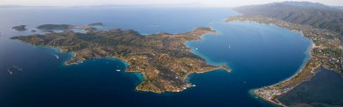 Yunanistan 'ın Sithonia Yarımadası' nda kristal berrak sularla çevrili plajları ve kayaları olan bir adanın havadan görünüşü. Yatlar ve tekneler turkuaz sularda demirliyor. Yakındaki adalar ve resifler görülebilir..