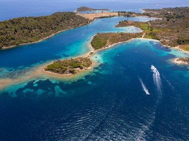 Yunanistan 'ın Sithonia Yarımadası' nda kristal berrak sularla çevrili plajları ve kayaları olan bir adanın havadan görünüşü. Yatlar ve tekneler turkuaz sularda demirliyor. Yakındaki adalar ve resifler görülebilir..